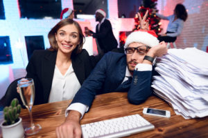 Office workers sitting at desk feeling overwhelmed by holiday celebrations.